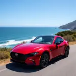 Thuê xe tự lái 4 chỗ Mazda theo ngày: Hình ảnh một chiếc Mazda đỏ đậu bên đường, sẵn sàng cho chuyến đi. Khung cảnh xung quanh là một con đường ven biển tuyệt đẹp.